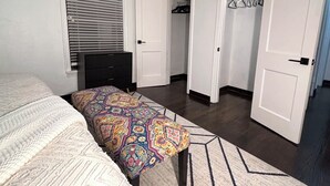 Een slaapkamer met een bed, een bankje, een radiator, een kast en een deur naar een andere kamer.