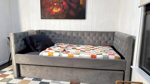 Een grijze, gestoffeerde bank met een geruit kleed en een donker kussen. Daarboven hangt een kleurrijk abstract schilderij.