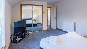 Una habitación de hotel con cama, televisor, espejo y puerta que da a otra habitación.