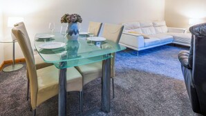 Una sala de estar moderna con una mesa de comedor de vidrio, sofás color beige y un jarrón decorativo.