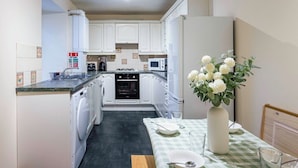 Una cocina compacta con armarios blancos, microondas, estufa y lavadora.