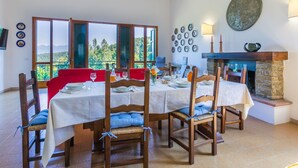 A dining area with a table set for four, wooden chairs with blue cushions, a stone fireplace, and a view of the outdoors through large windows. - Beautiful private villa for 10 people with A/C, WIFI, private pool and panoramic view (Vicchio)