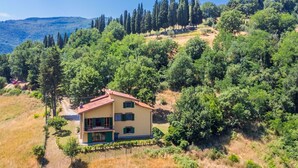 A two-story house with a red roof, surrounded by dense greenery and trees. - Beautiful private villa for 10 people with A/C, WIFI, private pool and panoramic view (Vicchio)