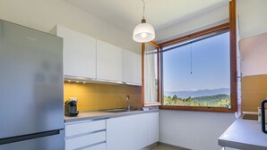A modern kitchen with white cabinets, a stainless steel refrigerator, a coffee maker, and a window with a view of a mountainous landscape. - Beautiful private villa for 10 people with A/C, WIFI, private pool and panoramic view (Vicchio)