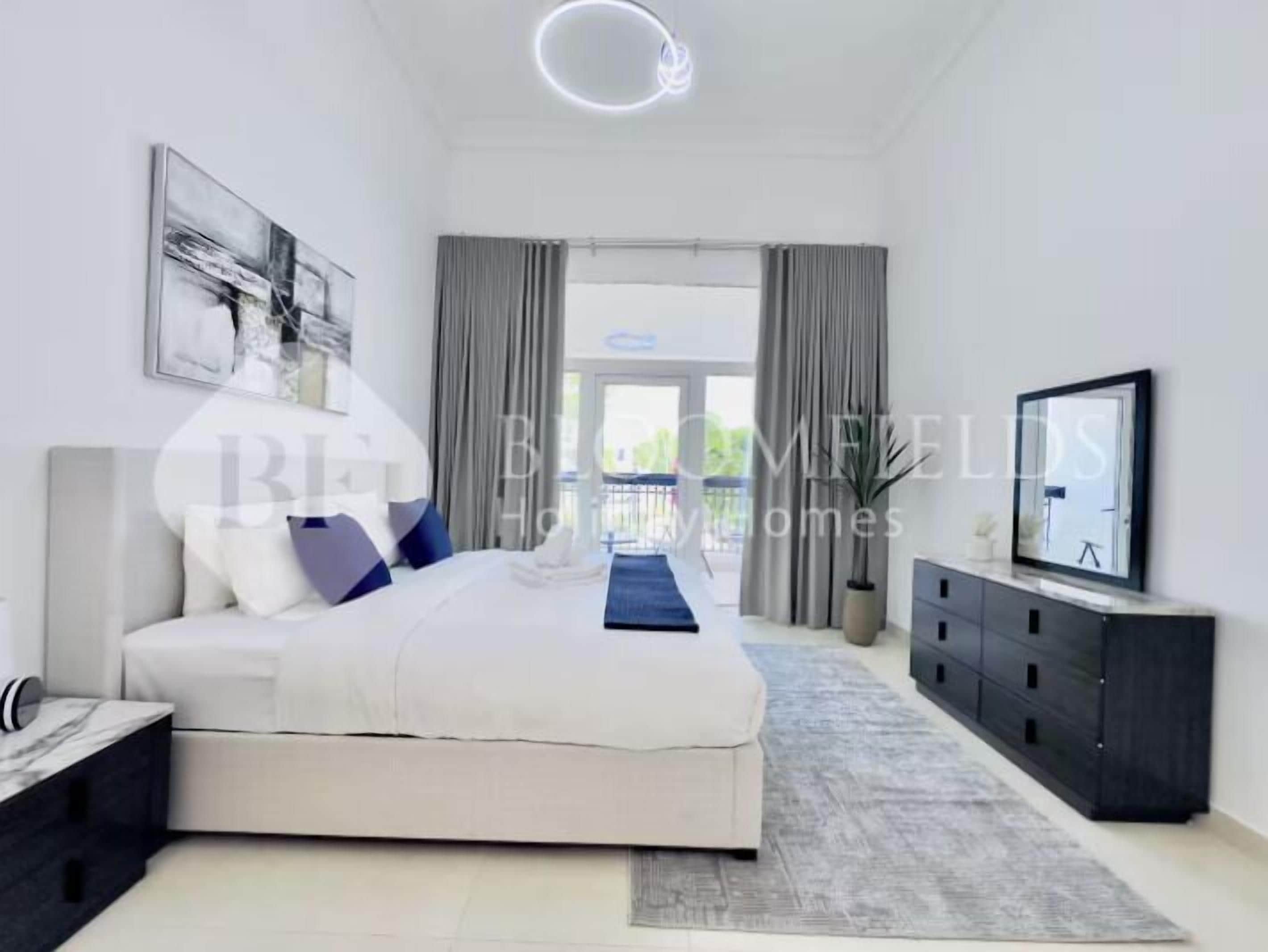 A modern bedroom with a bed, a TV, a desk, and a large window.