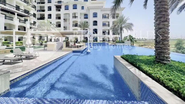 A hotel with a swimming pool, palm trees, and a multi-story building with balconies.