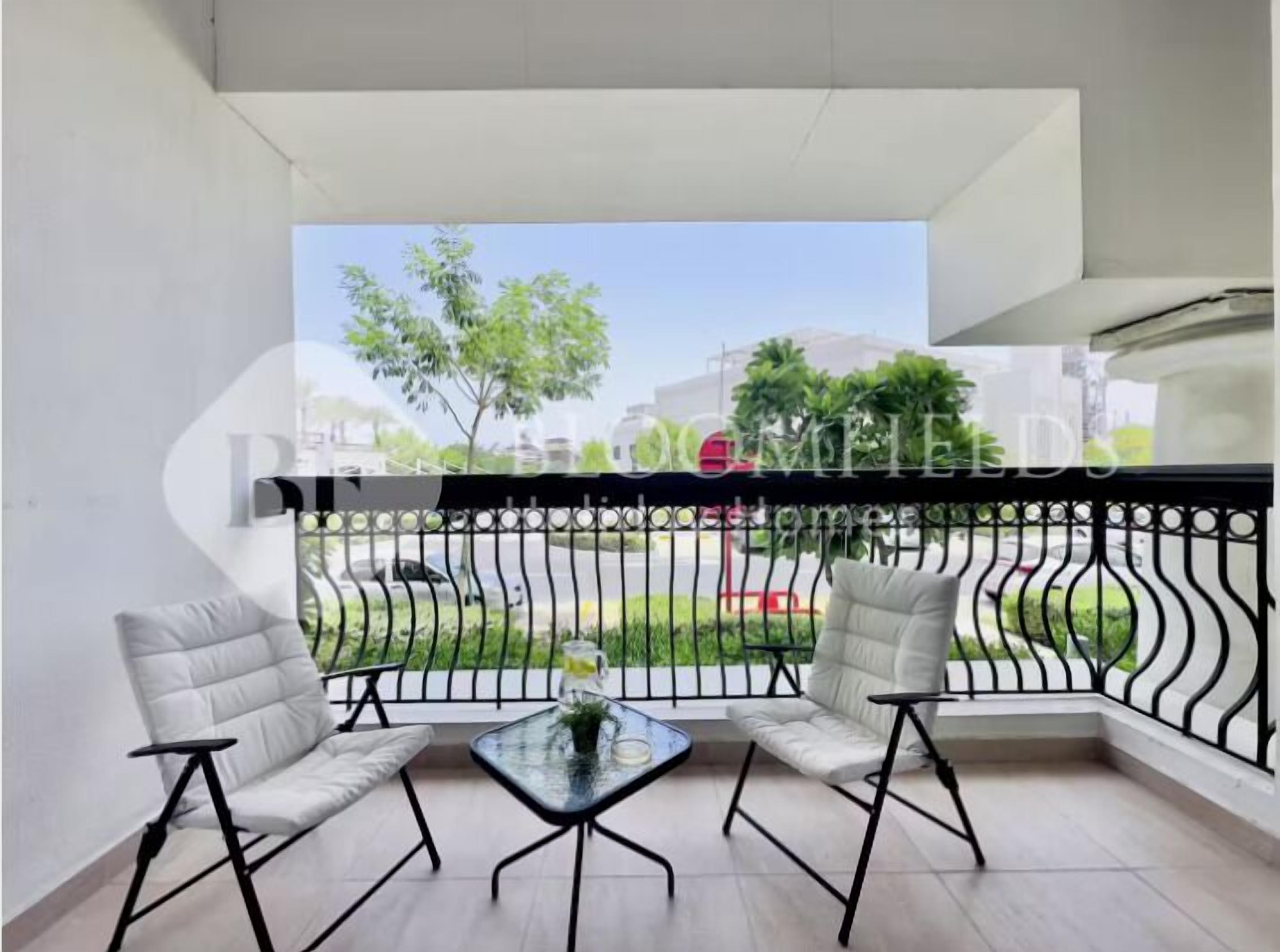 A balcony with two white cushioned chairs, a small glass table, and a black metal railing.