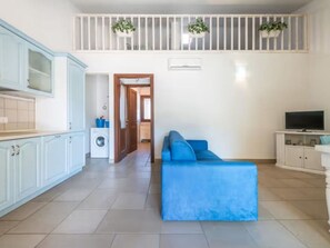 Eine moderne Wohnung mit Küche, einem Wohnbereich mit blauem Sofa, einem Fernseher und einem Balkon mit Pflanzen.