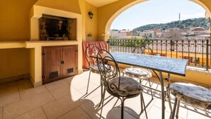 Un balcó amb taula i cadires, una barbacoa i vista a la ciutat.