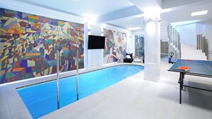 Un área de piscina interior moderna con arte abstracto en las paredes, una mesa de ping pong y una escalera que sube a otro nivel.