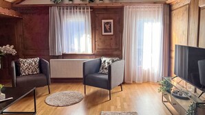 A cozy living room with a sofa, two armchairs, a coffee table, and a TV on a wooden cabinet. - Beautiful apartment for 7 people with WIFI, TV, balcony, pets allowed and panoramic view (Klosters Platz)
