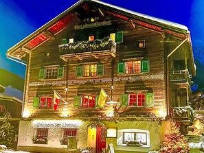 En traditionell byggnad i trä med flera fönster, några med gröna fönsterluckor, och en skylt som visar att det är en restaurang.