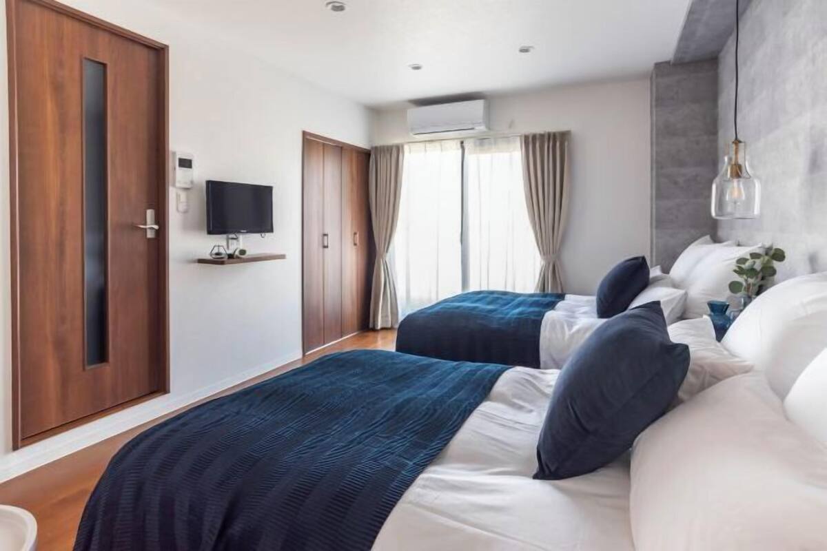 A hotel room with two beds, a TV, an air conditioning unit, and a wooden wardrobe.