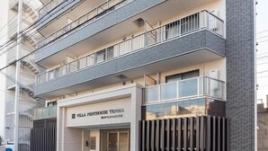 A multi-story building with a modern design, featuring balconies on each floor and a prominent entrance with a glass door. - Villa Penthouse Tenma (Osaka)