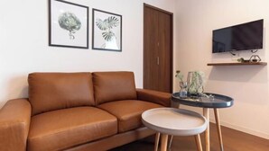 A brown leather sofa, a small round table with a white top, and a television mounted on the wall. - Villa Penthouse Tenma (Osaka)