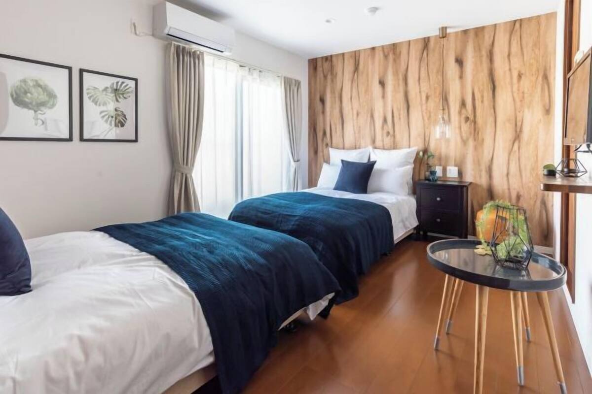 A hotel room with two beds, a wooden accent wall, a small round table, and a plant.