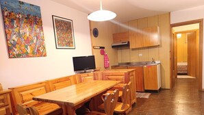 Una mesa de comedor de madera con sillas, un televisor y armarios de madera en una habitación con suelo de ladrillo.