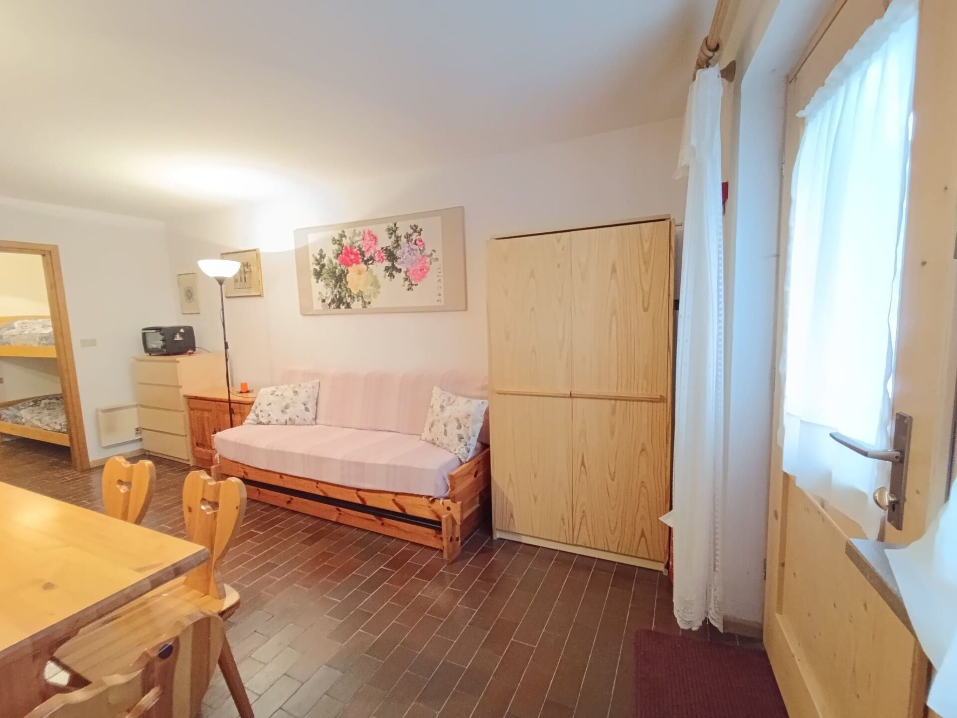 Um quarto aconchegante com sofá de madeira, guarda-roupa de madeira, uma mesa de jantar com cadeiras e uma pequena escrivaninha com abajur.