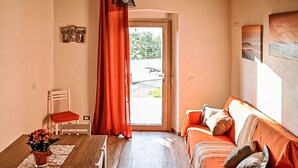 Een gezellige kamer met een houten eettafel, een rode bank en een stoel. Er is een raam met uitzicht op groen.
