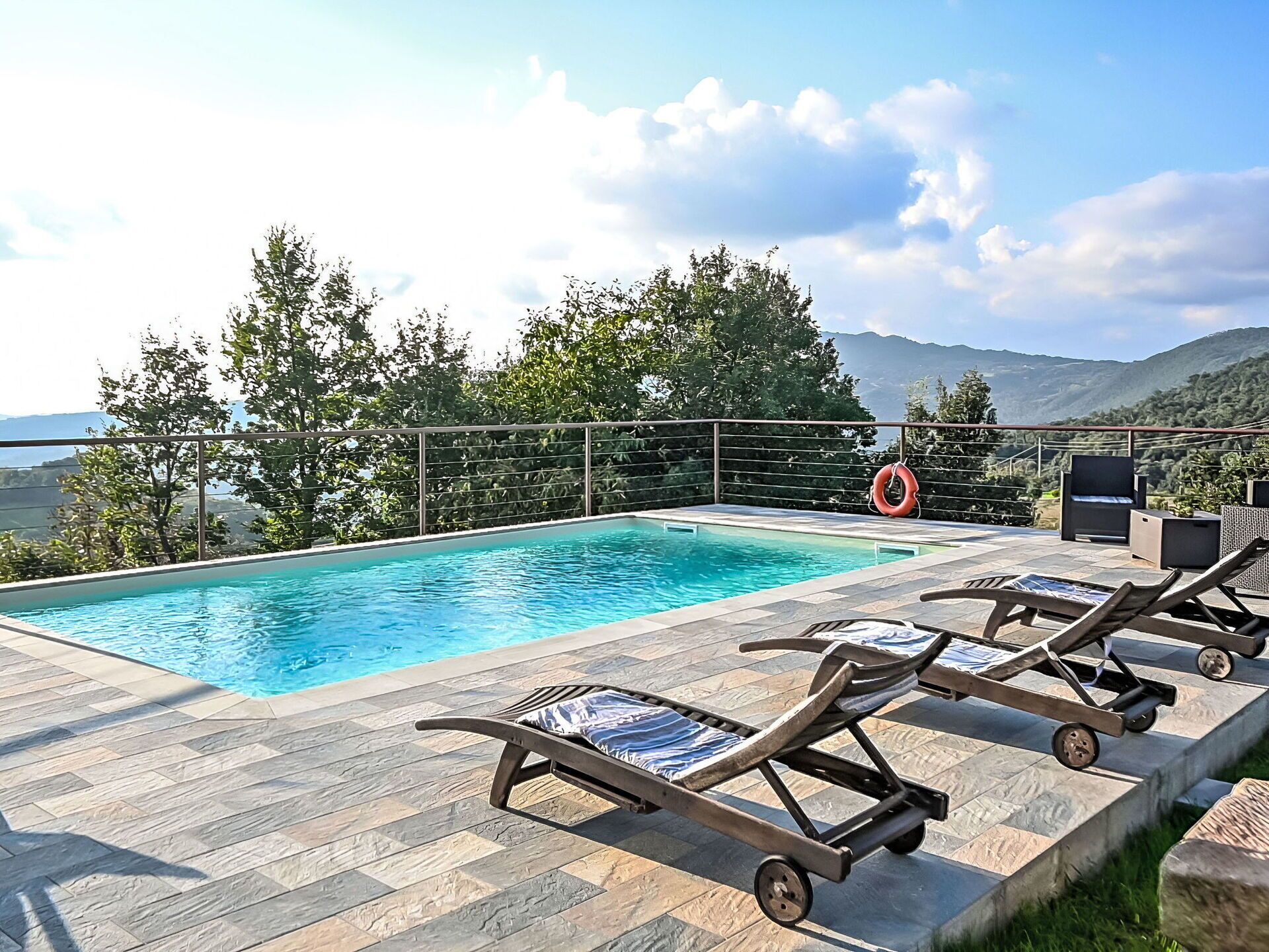 A poolside area with lounge chairs, a lifebuoy, and a view of mountains.
