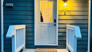 A small, dark-colored building with a white door and a number '2' on the wall. - The Nook at Latimer - 2 Bedroom Carriage House- Short Walk to Downtown and Beach (Penticton)