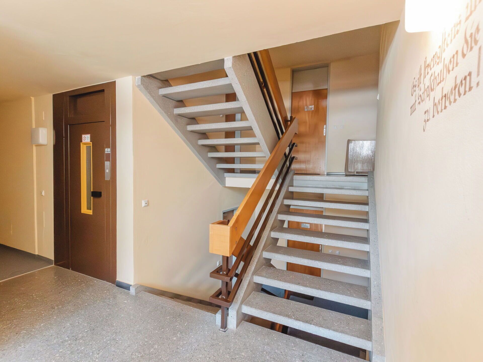 A modern interior with a wooden staircase, a door with a sign, and a wall with text.