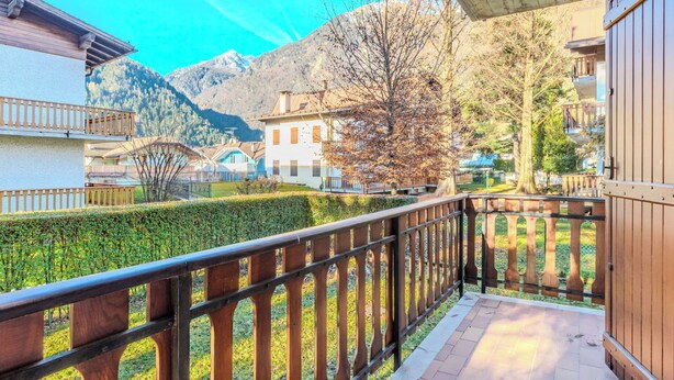 Ein Balkon mit Holzgeländer, der einen ordentlich gestutzten Heckenstreifen und einen Blick auf die Berge bietet.