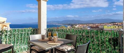 A balcony with a table and chairs, a view of the sea, and a distant town.