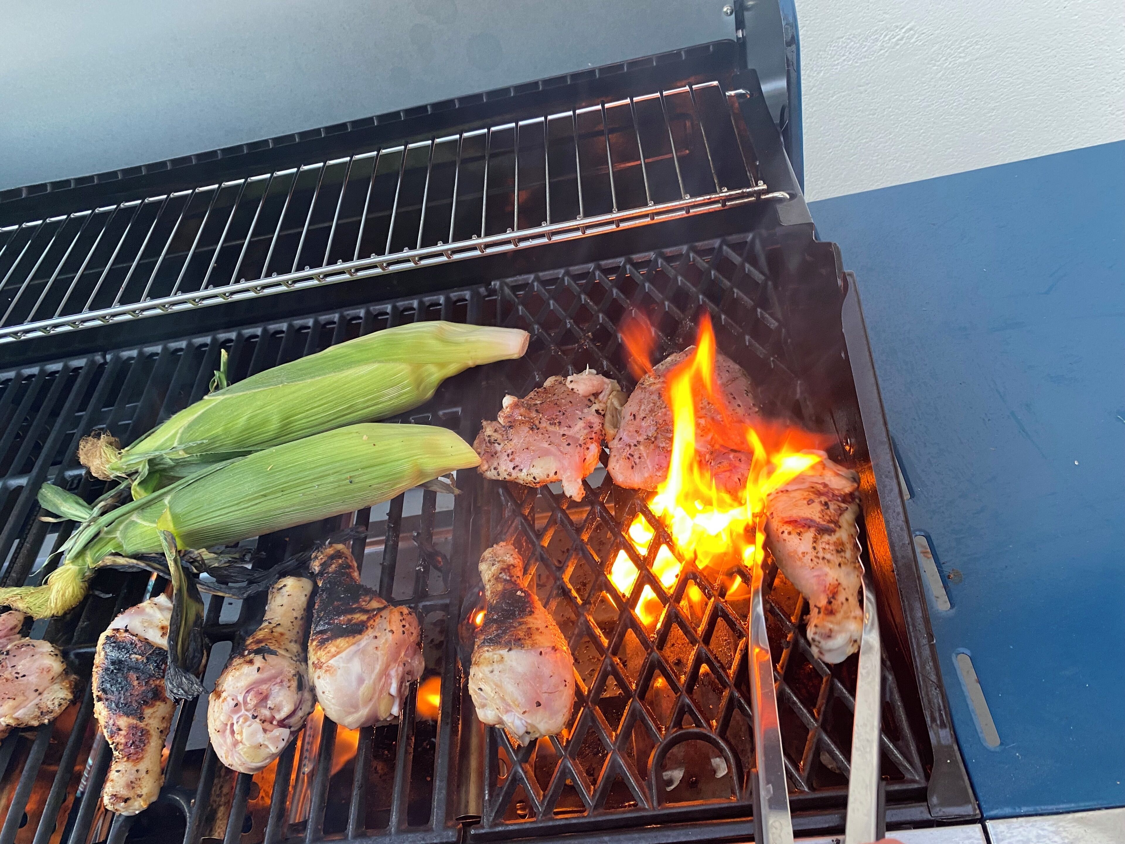 Een barbecue met kip en mais die boven een open vuur wordt bereid.