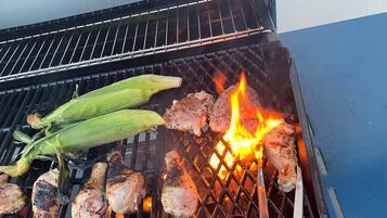 Een barbecue met kip en mais die boven een open vuur wordt bereid.