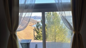 Finestra amb cortines lleugeres, vista d'un paisatge de muntanya i una taula amb un ordinador portàtil.
