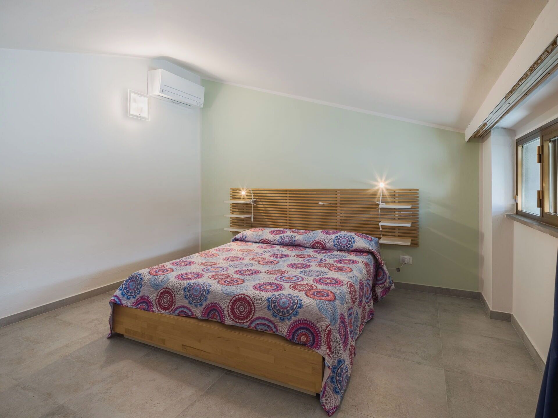 Une chambre à coucher avec un lit en bois, une literie à motifs, une tête de lit à lattes et une fenêtre avec des stores.