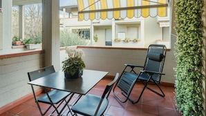 Un patio cubierto con mesa y sillas, plantas en macetas y un toldo a rayas amarillas.