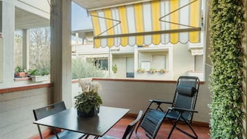 A covered patio area with a table and chairs, potted plants, and a yellow-striped awning.