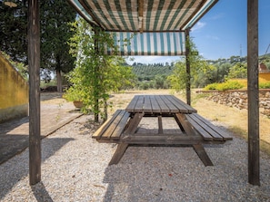 Ein Holztisch mit Picknickatmosphäre unter einem gestreiften Baldachin, umgeben von Kies und Grünpflanzen.
