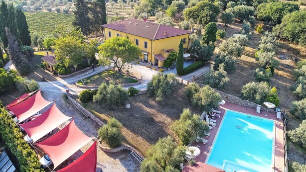 Una villa amarilla con piscina, rodeada de olivares y toldos rojos.
