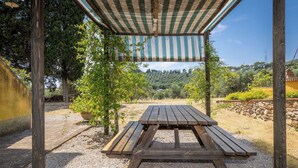 A wooden picnic table under a striped awning, surrounded by gravel and greenery. - Nice apartment for 3 people with WIFI, A/C, pool, terrace, pets allowed and panoramic view (Campiglia Marittima)