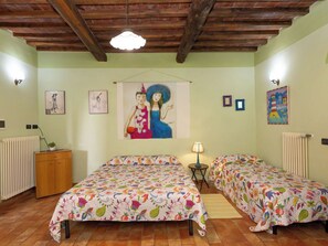 A room with two beds, a wooden cabinet, a radiator, and a hanging light fixture.