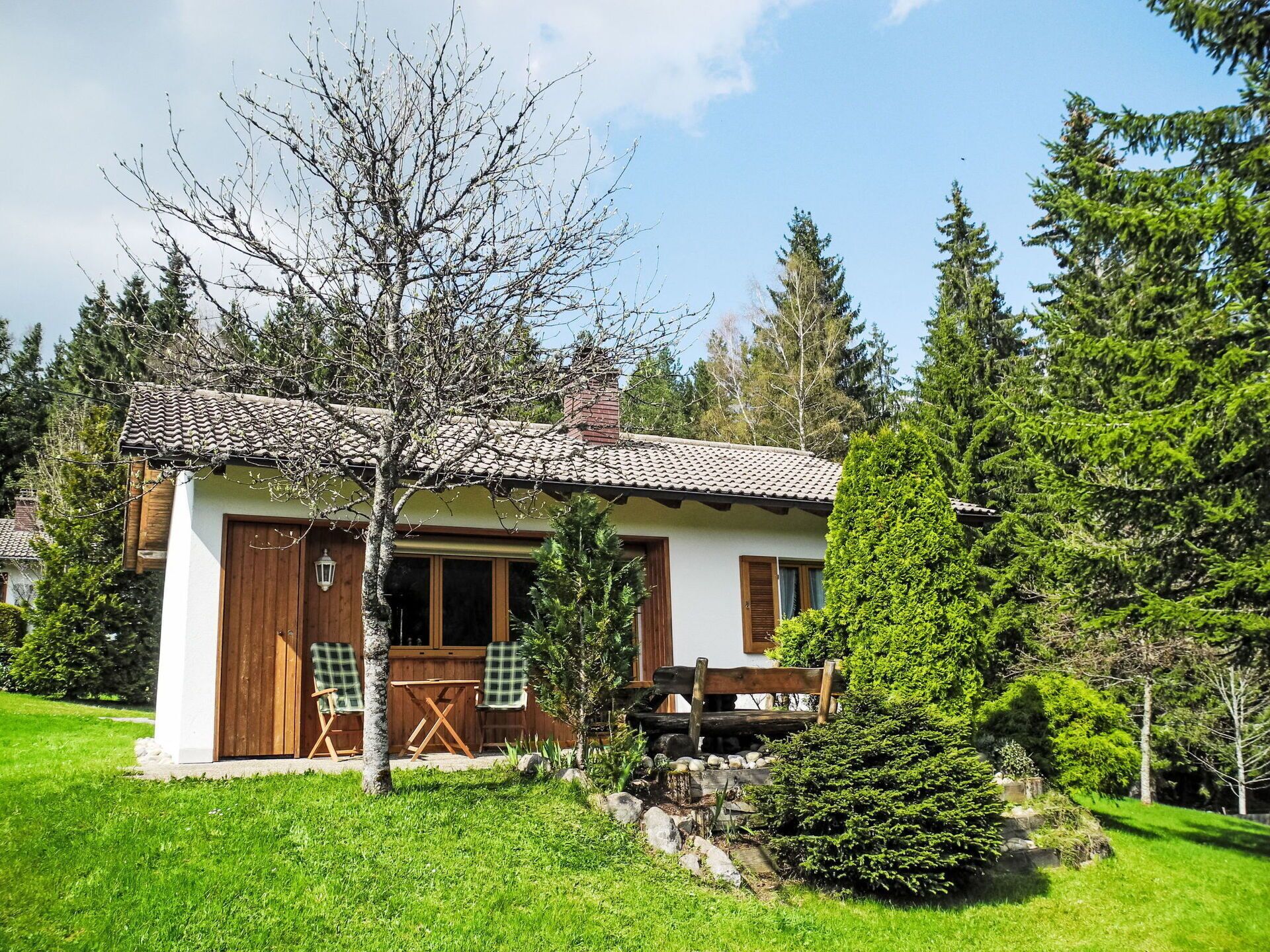 Ein kleines, eingeschossiges Haus mit einem Ziegeldach, einer Holztür und einer kleinen Veranda mit einer Bank.