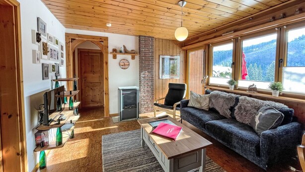 Ein gemütliches Wohnzimmer mit Holzbalkendecke, einer Couch, einem Couchtisch und einem Kamin.