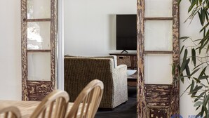 Ein Zimmer mit Esstisch und Stühlen, einem Korbsessel und einem Fernseher auf einem Schrank.