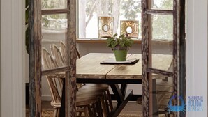 Ein Holzespeisetisch mit Stühlen, ein grünes Kübelpflänzchen und zwei dekorative Holzpaneele auf einer Fensterbank.