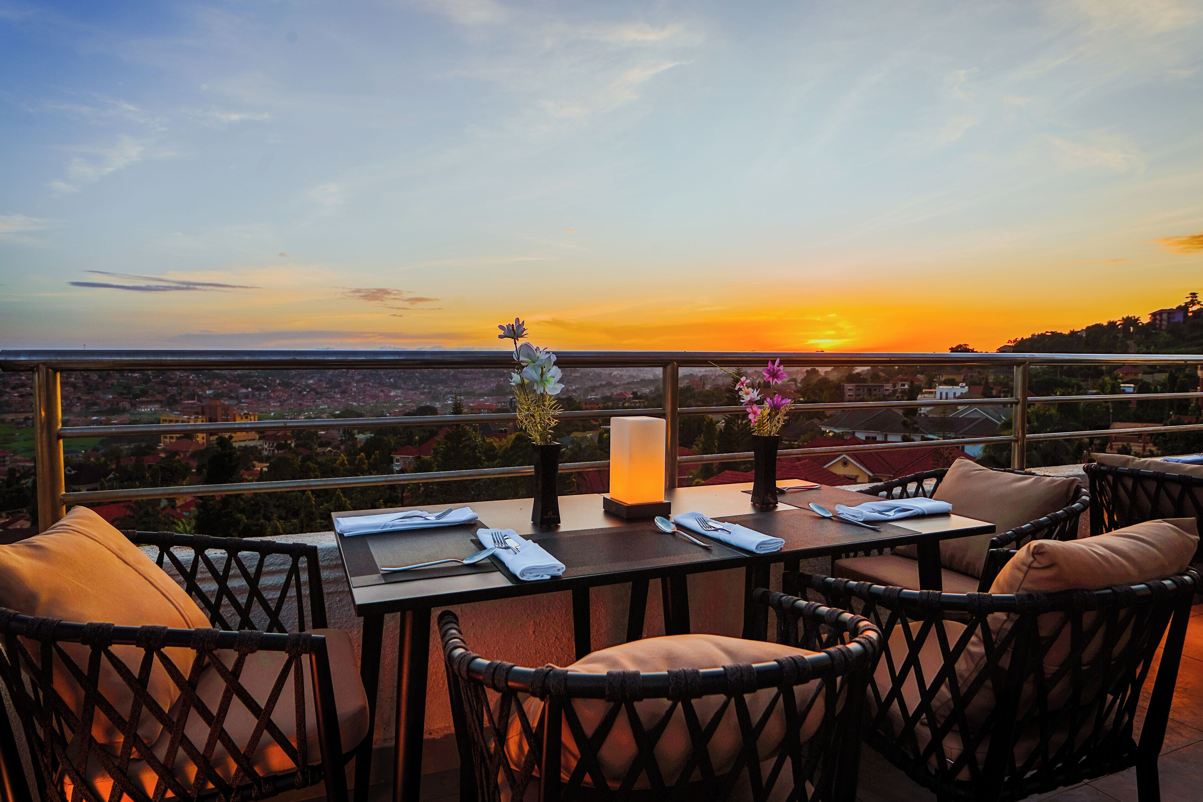 Uma área de refeições com uma mesa posta para dois, com vista para um horizonte urbano ao pôr do sol.
