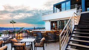 An outdoor terrace with seating and a bar area, overlooking a scenic landscape. - Hotel Noesis  (Kampala)