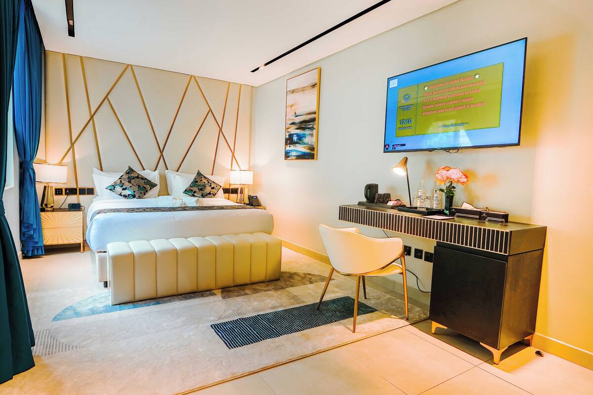 A modern hotel room with a bed, bedside tables, a desk, and a TV displaying a welcome message.