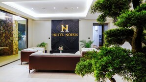 A modern hotel lobby with a reception desk, a sofa, and a large potted tree. - Hotel Noesis  (Kampala)