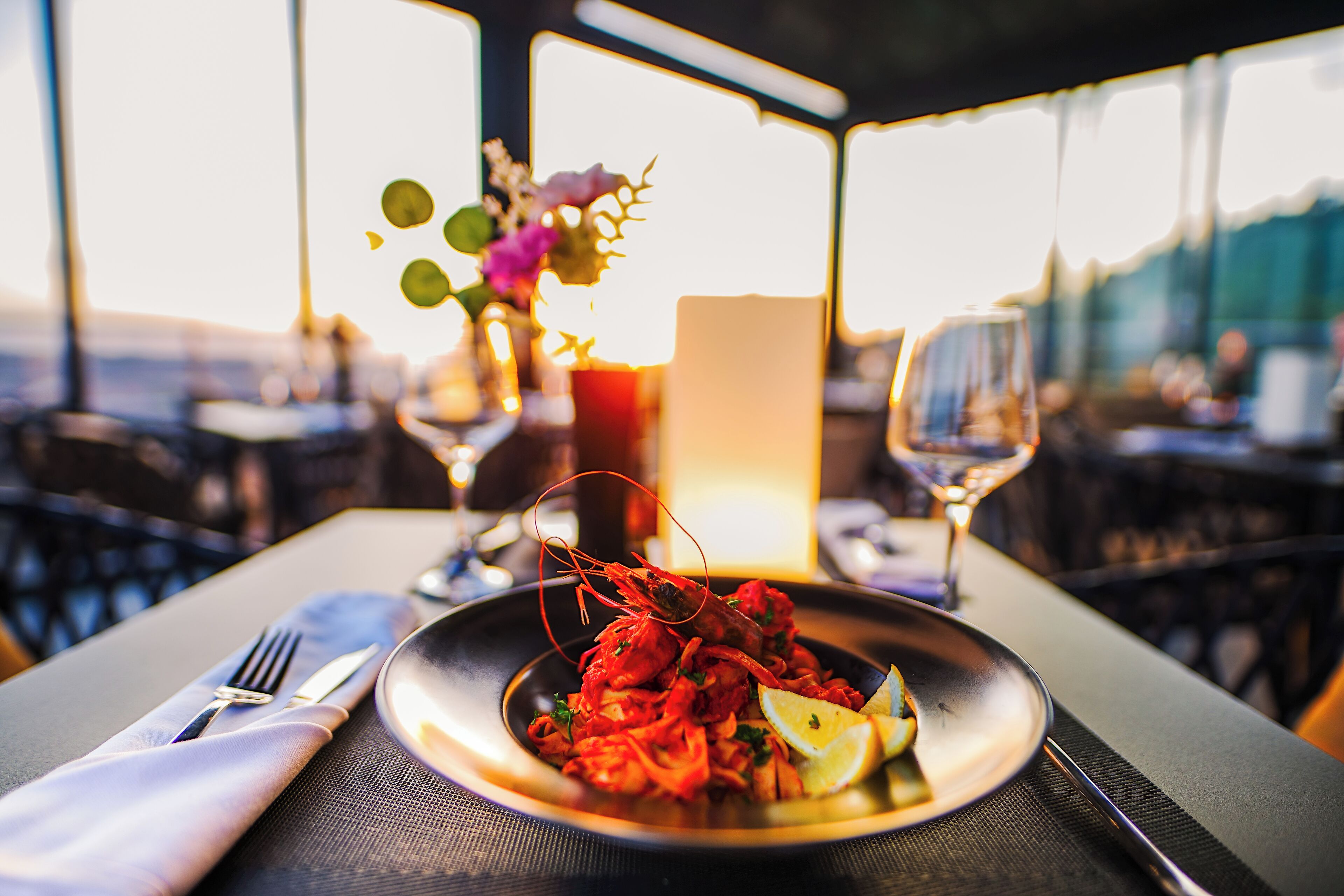 A dining table with a seafood dish, a glass of wine, and a vase with flowers.