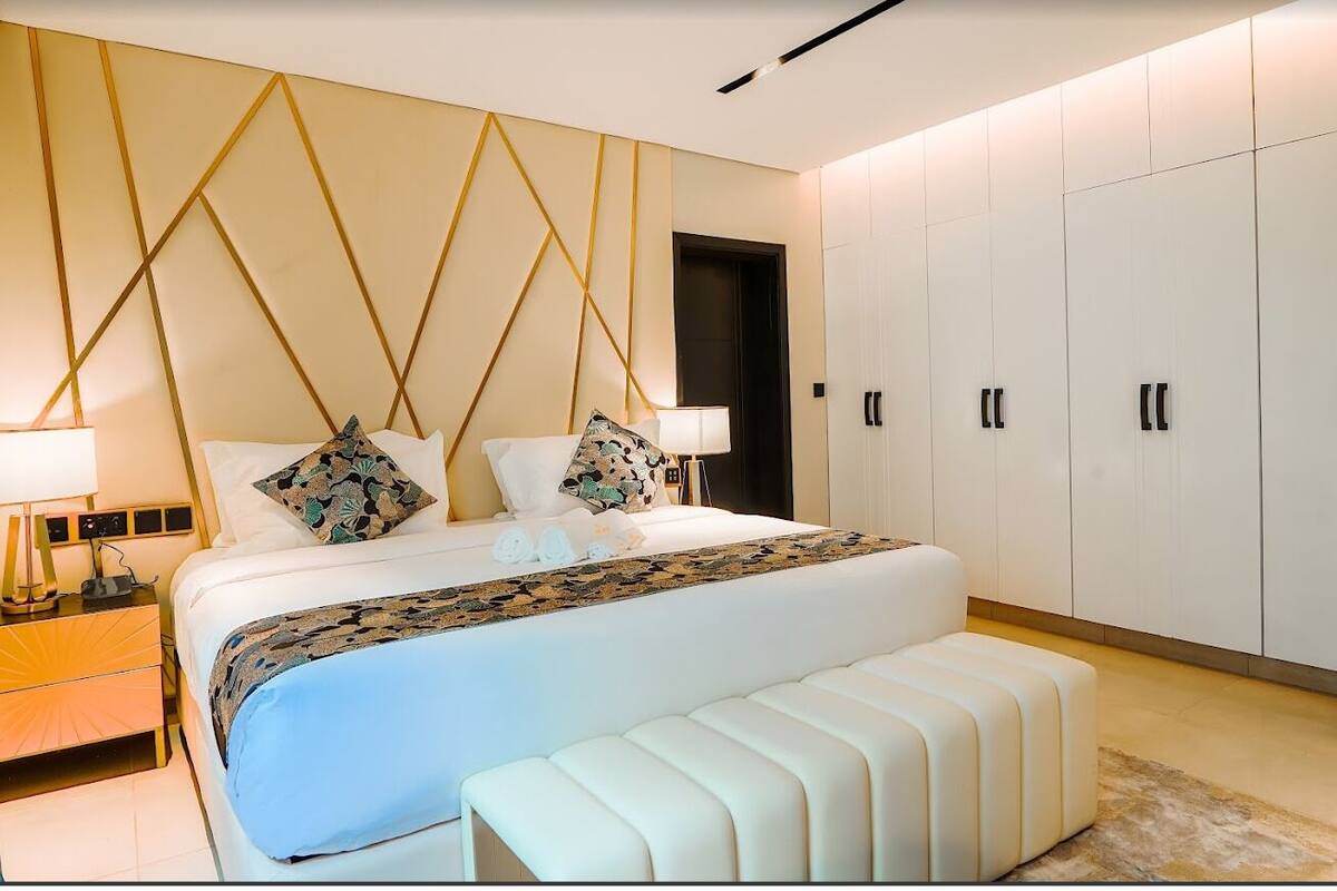 A modern bedroom with a large bed, bedside tables, a bench, and a wardrobe.