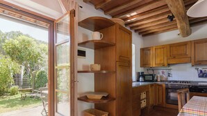 A kitchen with wooden cabinets, a dining table with a checkered tablecloth, and a view of the garden through a glass door. - Cosy apartment for 4 people with WIFI, TV, patio, pets allowed and panoramic view (Gavorrano)