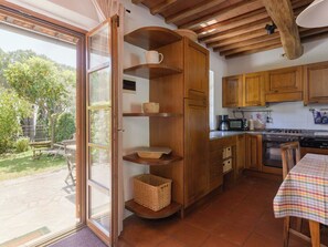 A kitchen with wooden cabinets, a dining table with a checkered tablecloth, and a view of the garden through a glass door. - Lovely apartment for 4 guests with WIFI, TV, patio, pets allowed and panoramic view (Gavorrano)